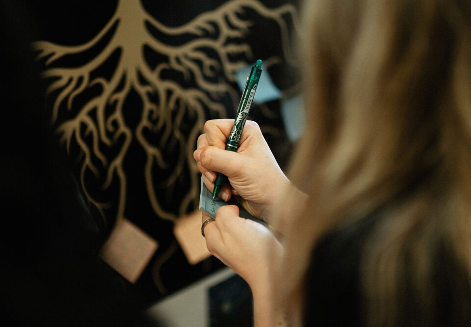 Person writing on a sticky note with a green pen.